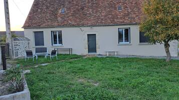 A two-story house with a tiled roof, a small front garden, and a bench.