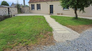 Une maison avec un toit en tuiles, un mur en pierre et un chemin de gravier menant à l’entrée.