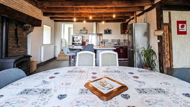 Une cuisine rustique avec des poutres apparentes, un îlot central et un coin repas agrémenté d’une nappe à motifs.
