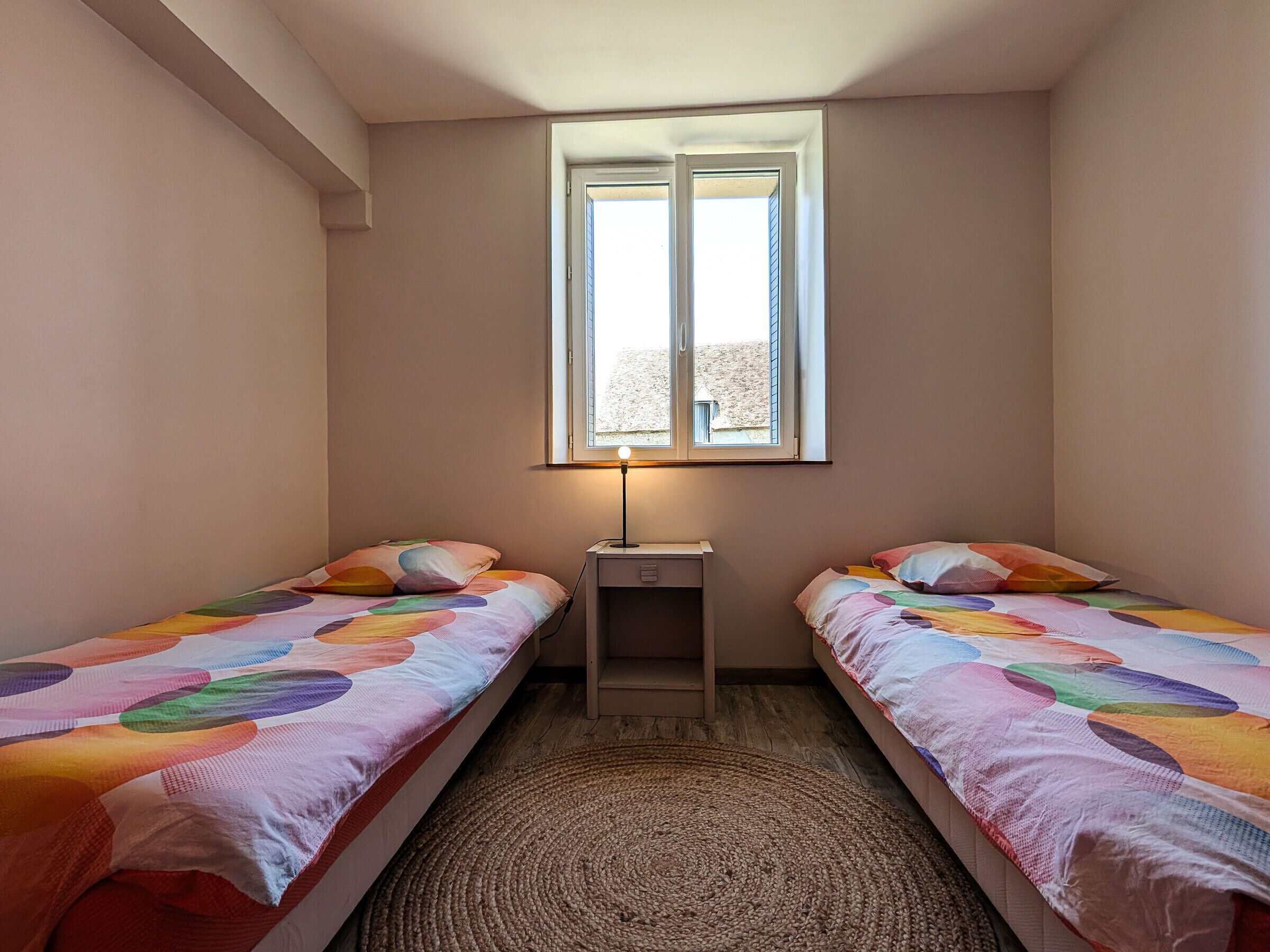 A small room with two single beds, a small table, and a window.
