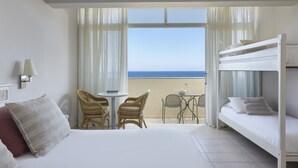 Une chambre d’hôtel avec un lit, une petite table, deux chaises, un balcon avec vue sur la mer et un lit superposé.