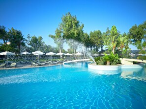 Ein Schwimmbecken mit Wasserspielen, Liegestühlen und Sonnenschirmen.