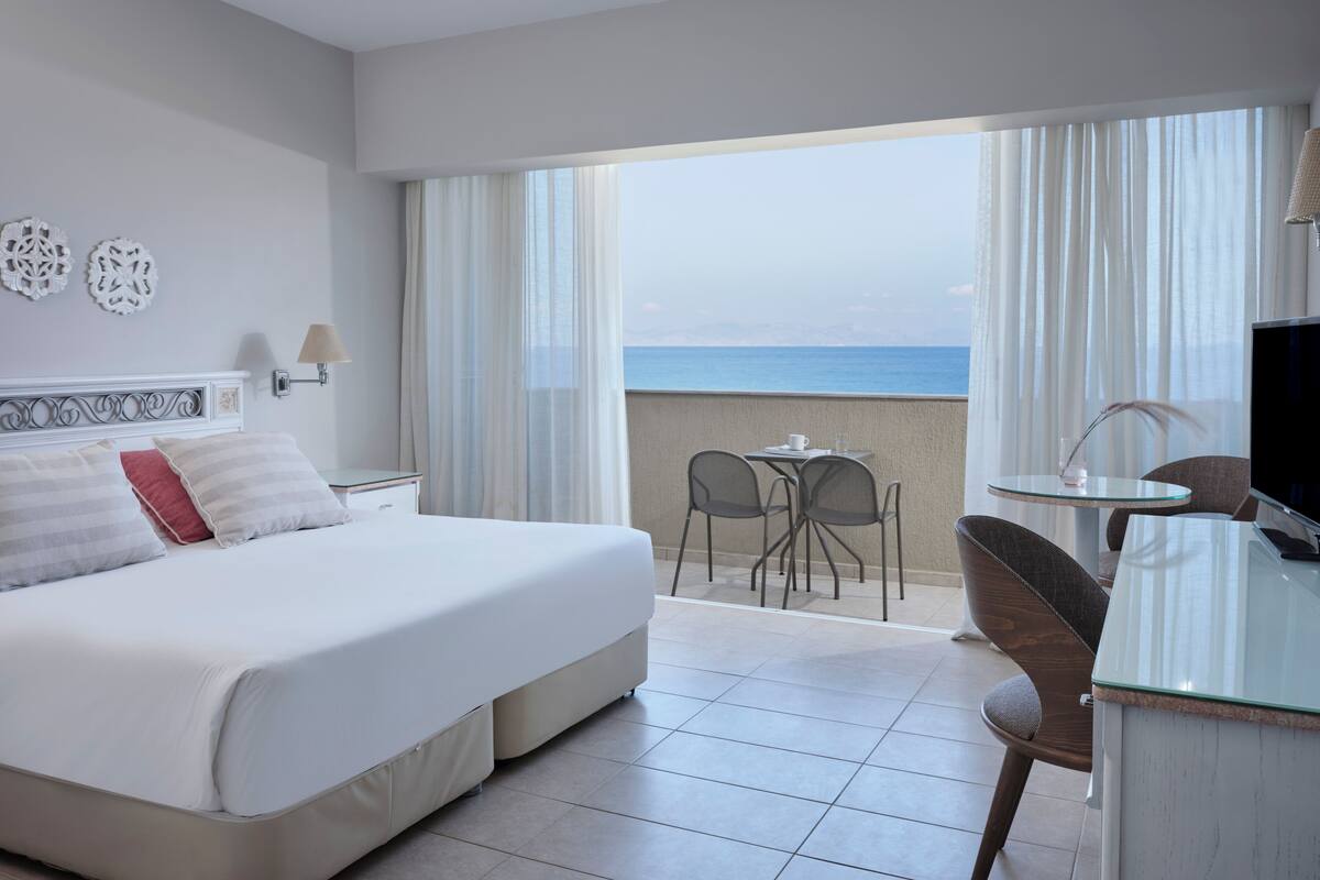 Een hotelkamer met een groot bed, een bureau, een stoel en uitzicht op zee.