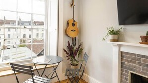 A room with a large window, a guitar, a TV, a fireplace, and a table with chairs. - Stylish Flat on Beautiful Clifton Street, Parking (Clifton)