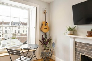 A room with a large window, a guitar, a TV, a fireplace, and a table with chairs. - Stylish Flat on Beautiful Clifton Street, Parking (Clifton)