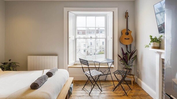 A bedroom with a bed, a window, a guitar, and a small table with chairs. - Stylish Flat on Beautiful Clifton Street, Parking (Clifton)
