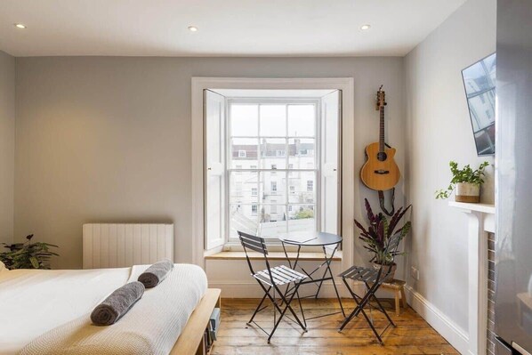 A bedroom with a bed, a window, a guitar, and a small table with chairs. - Stylish Flat on Beautiful Clifton Street, Parking (Clifton)