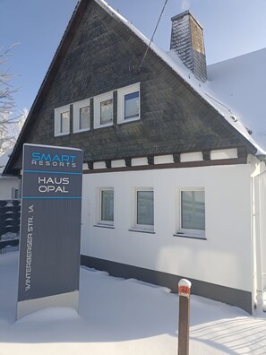 Un edificio de dos pisos con techo nevado y un letrero que dice Smart Resort Haus Opal.
