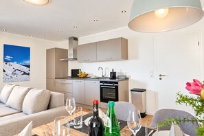 Una cocina moderna con horno empotrado, un comedor con mesa para dos, y un sofá en la sala de estar.