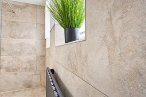 Un baño con suelo de baldosas, un radiador y una planta en maceta en la pared.
