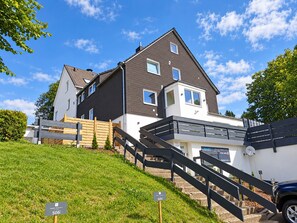 Ein zweistöckiges Haus mit modernem Design, einer sichtbaren Treppe und einem gepflegten Rasen.