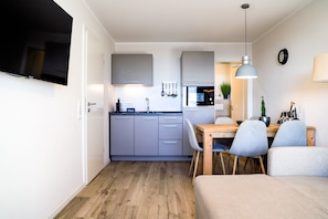 Cocina compacta con armarios grises, un microondas y un comedor con mesa de madera y sillas grises.