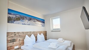 Een slaapkamer met een houten hoofdbord, wit beddengoed, een raam en een groot landschap op de muur.