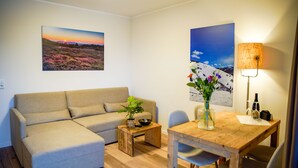 Un salon comprenant un canapé, une table basse en bois ornée d’une plante, une table à manger avec des chaises et deux tableaux accrochés au mur.