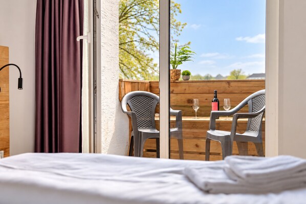 A bedroom with a bed, a window with curtains, and a view of a wooden deck with chairs and a table.