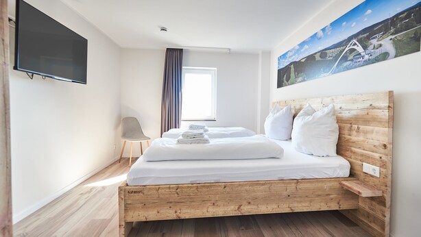 A modern hotel room with a wooden bed, a flat-screen TV, a window with curtains, and a painting on the wall. - Smart Resorts - Haus Saphir - Ferienwohnung 506 mit 2 Schlafzimmern, max (Winterberg)
