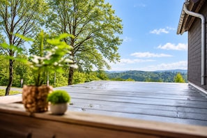 A wooden deck with potted plants, overlooking a forested landscape and distant hills.