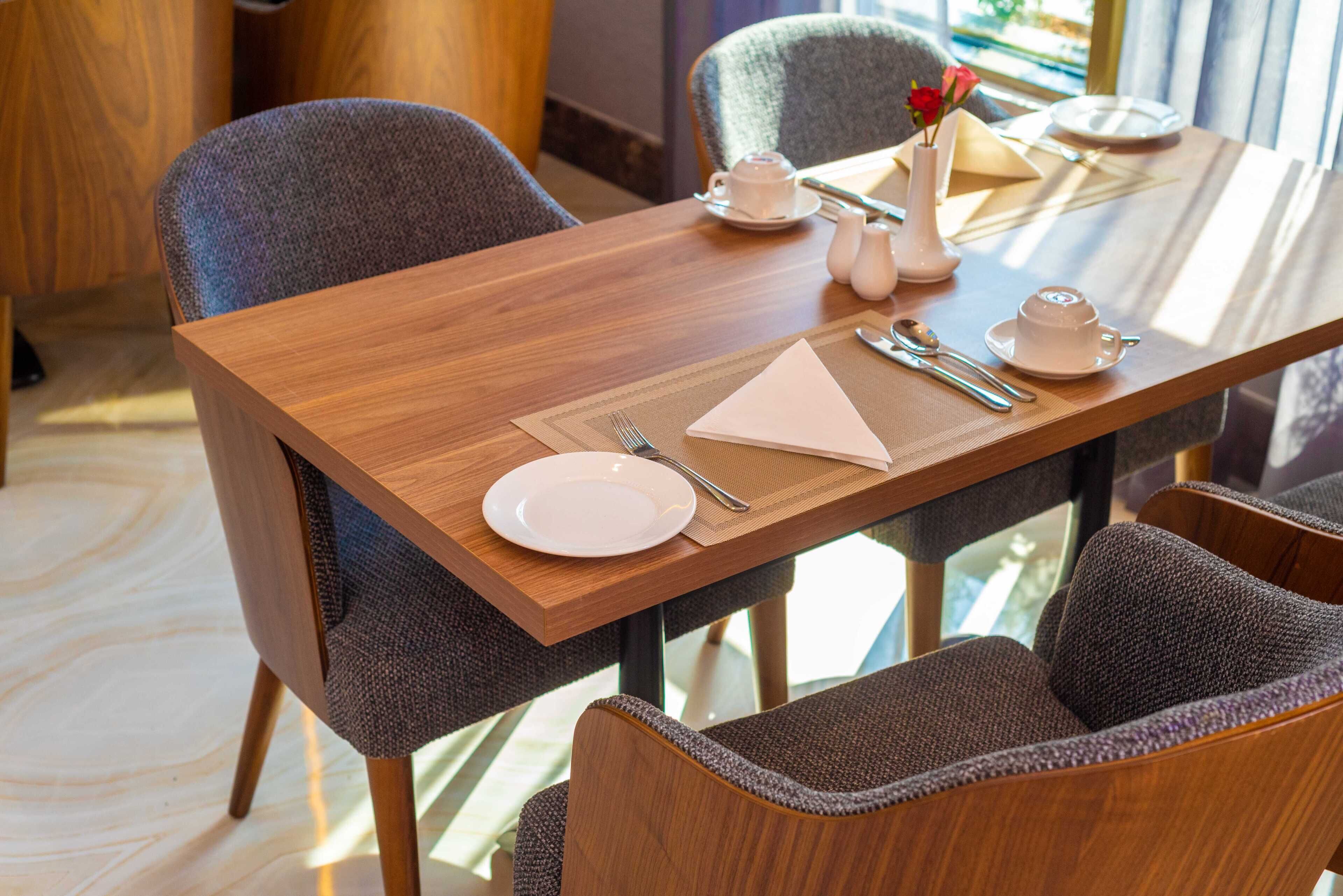 A dining table set with a white plate, silverware, a napkin, and a teapot.