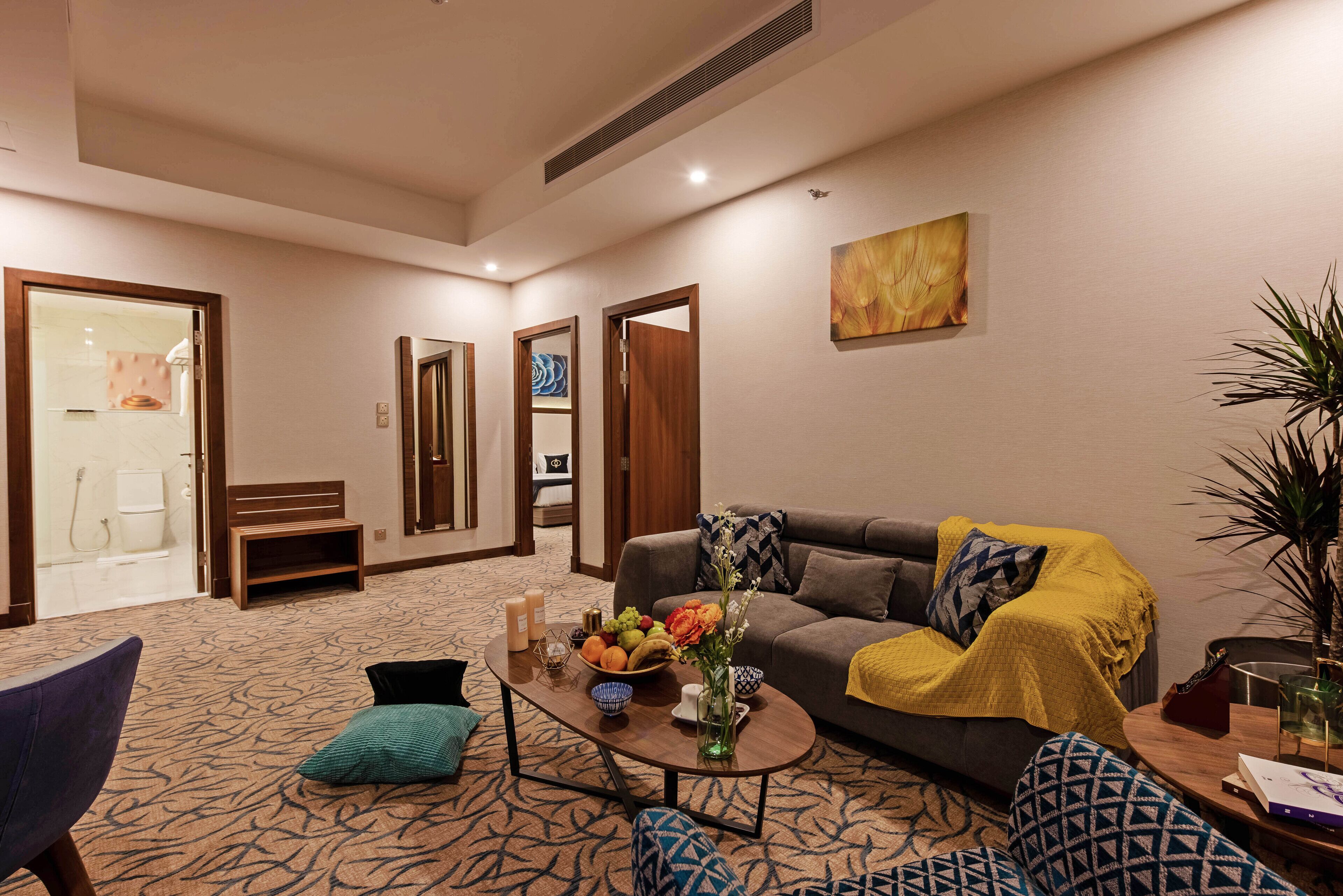 A modern living room with a grey sofa, a coffee table with a vase and fruit bowl, and a patterned carpet.