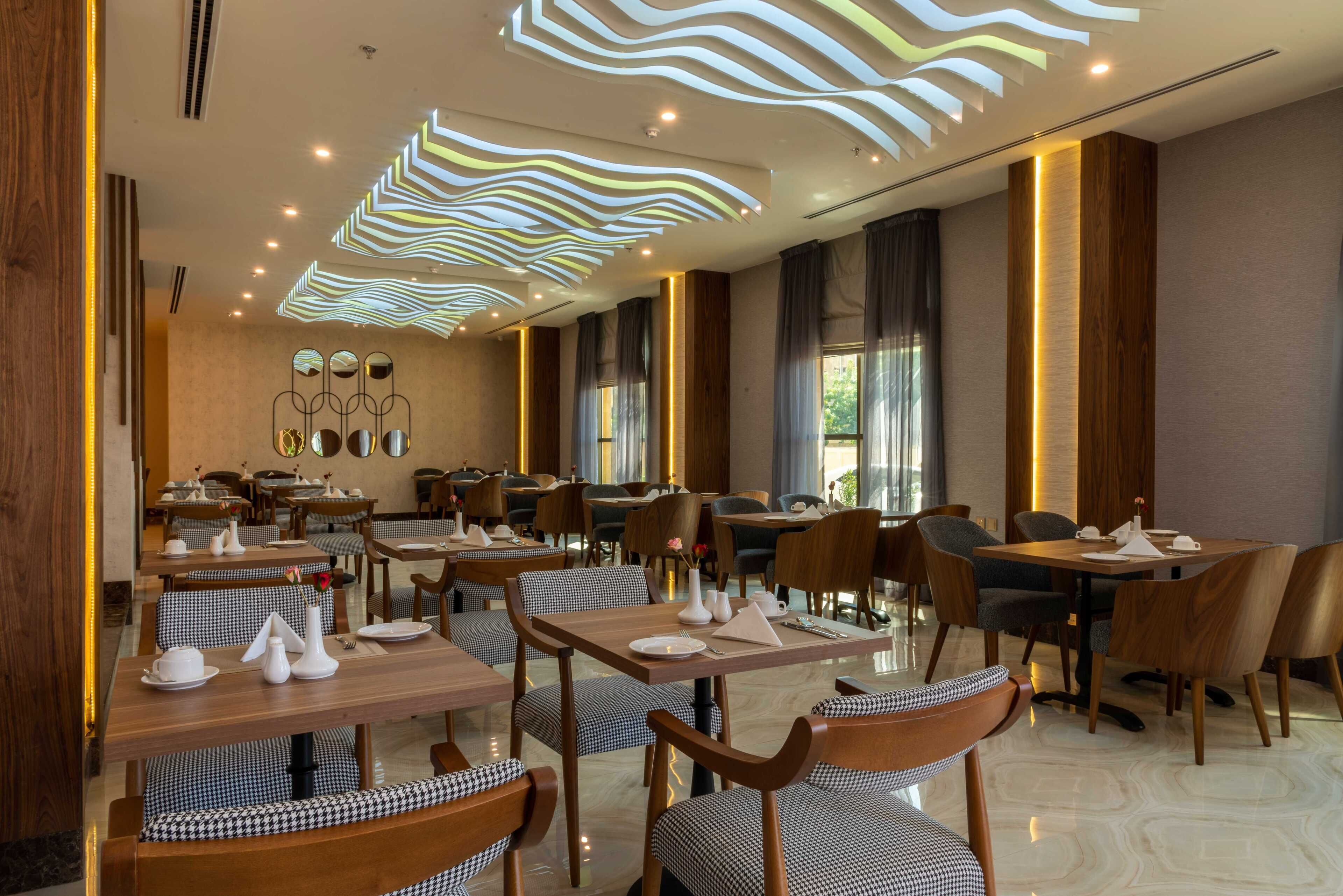 A modern dining area with wooden tables and chairs, a patterned ceiling design, and large windows allowing natural light.