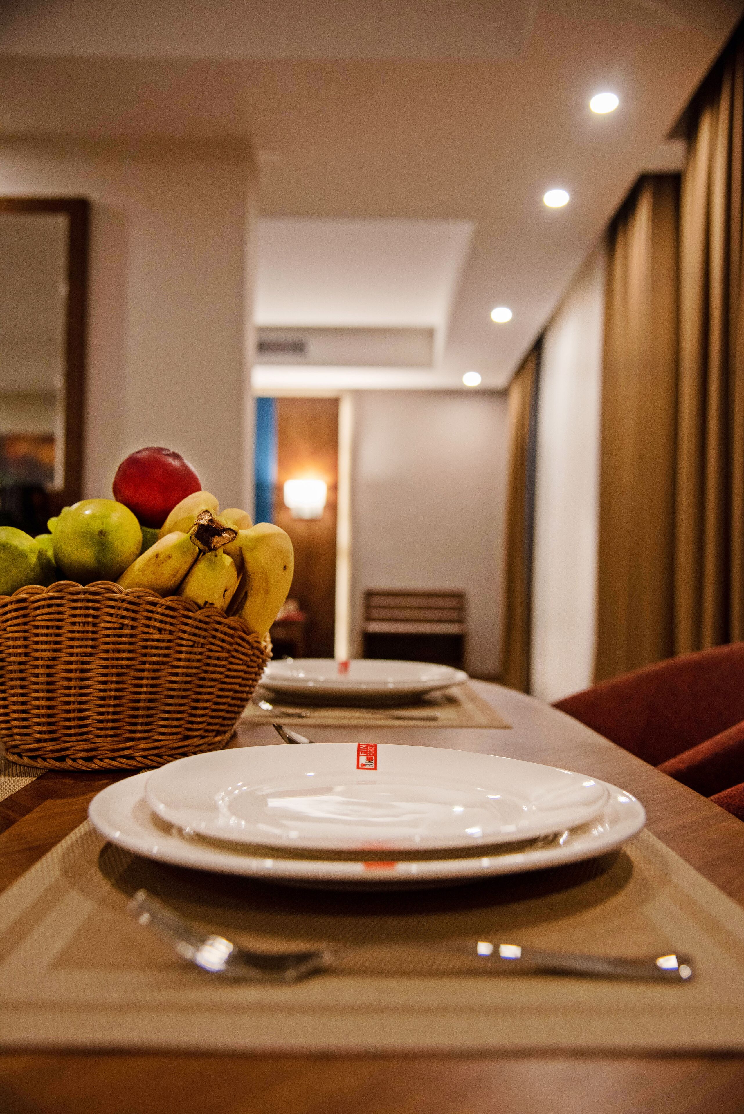 Una mesa lista con platos, una cesta de fruta y un posavasos.