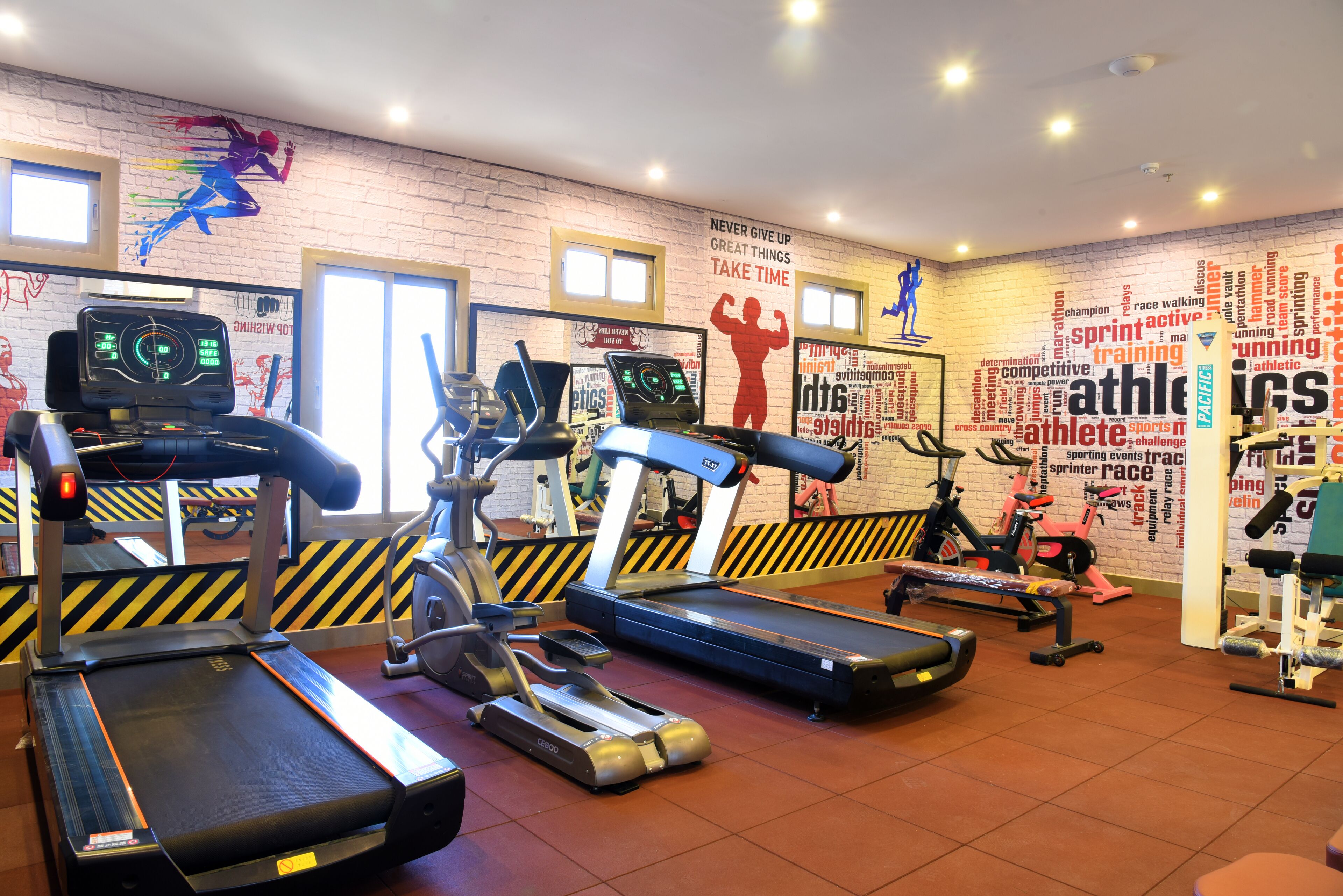 A gym with treadmills, ellipticals, and a wall with motivational sports-related words and phrases.