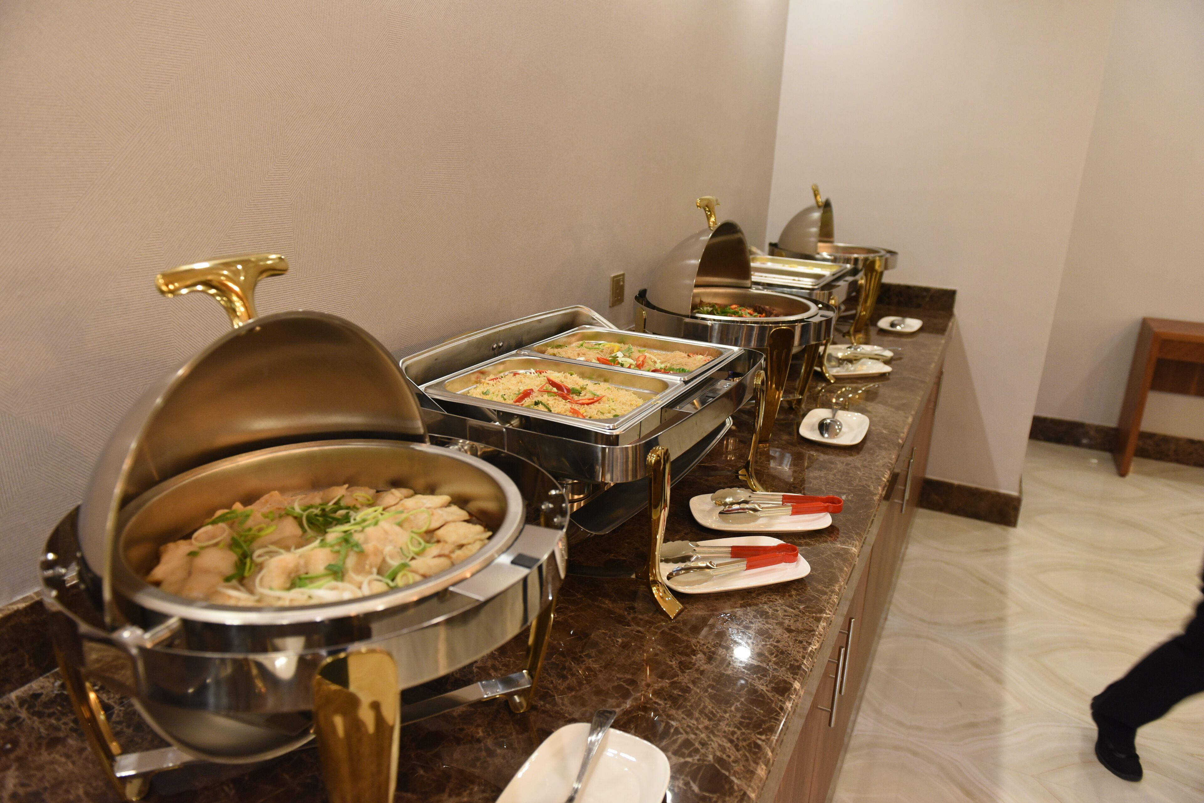 A buffet setup with various food containers and serving utensils.