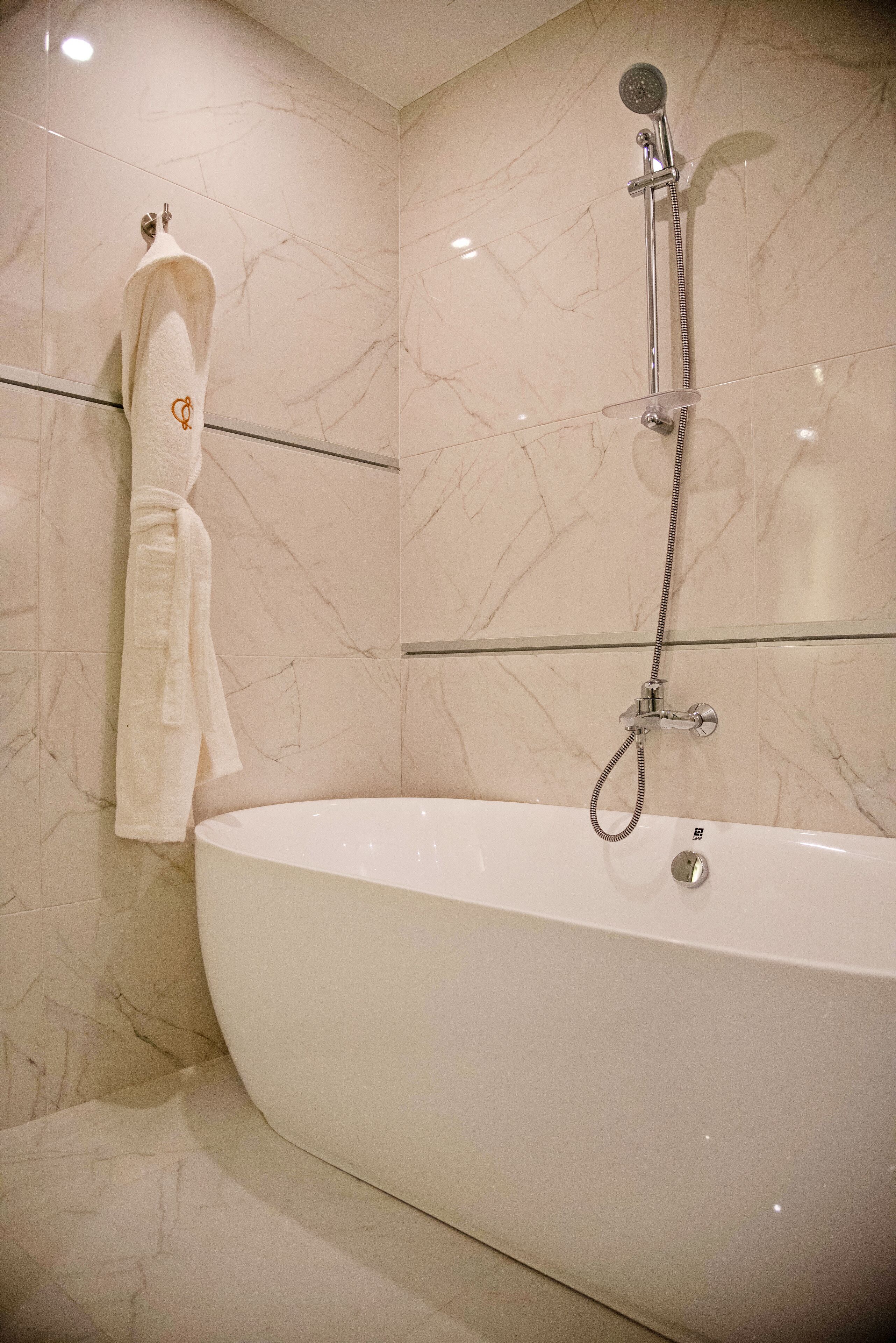 A modern bathroom with a freestanding bathtub, a handheld showerhead, and a towel rack with a white towel.