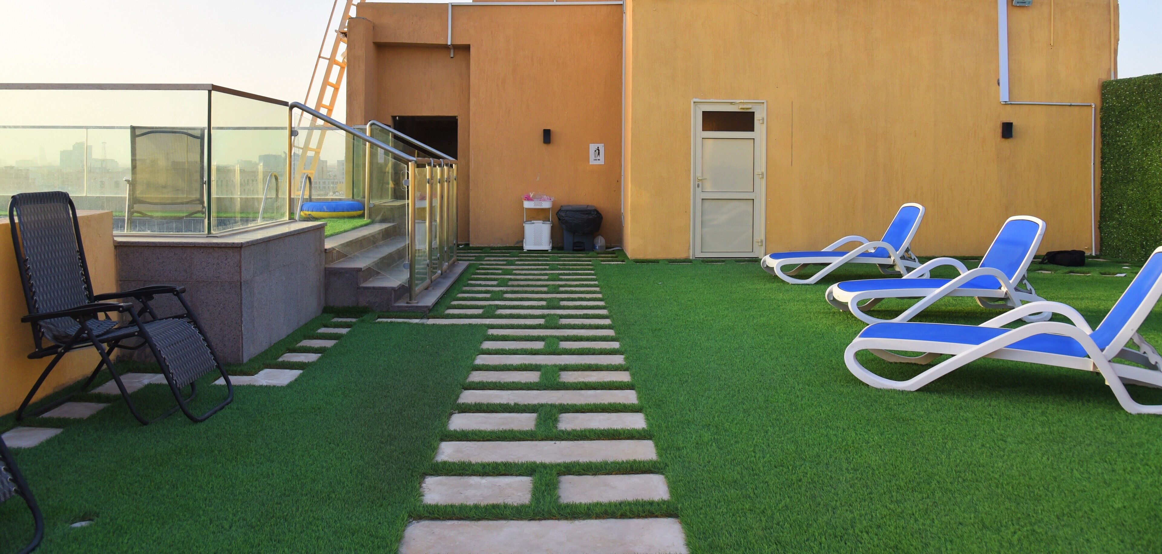 Una terraza en la azotea con césped artificial, barandilla de vidrio y sillones de descanso.