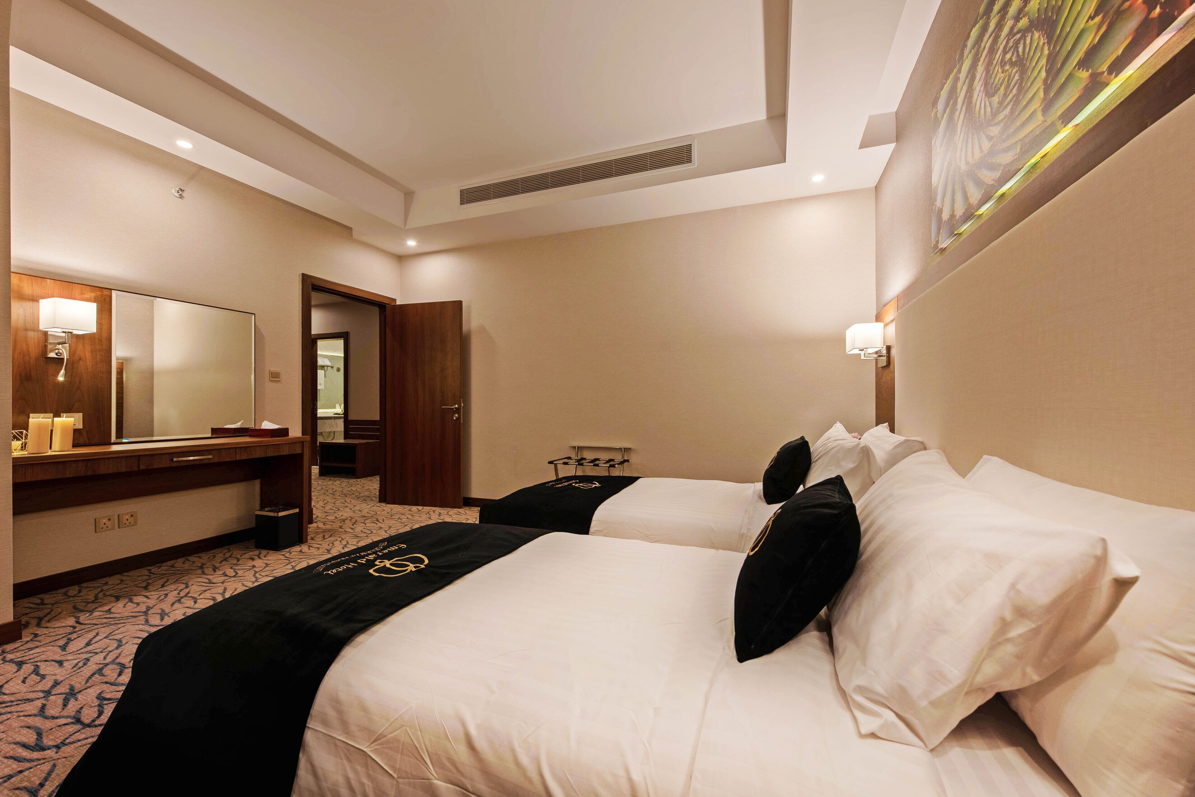 Een hotelkamer met twee bedden, een grote spiegel, een kaptafel met een lamp en een deur naar een andere kamer.