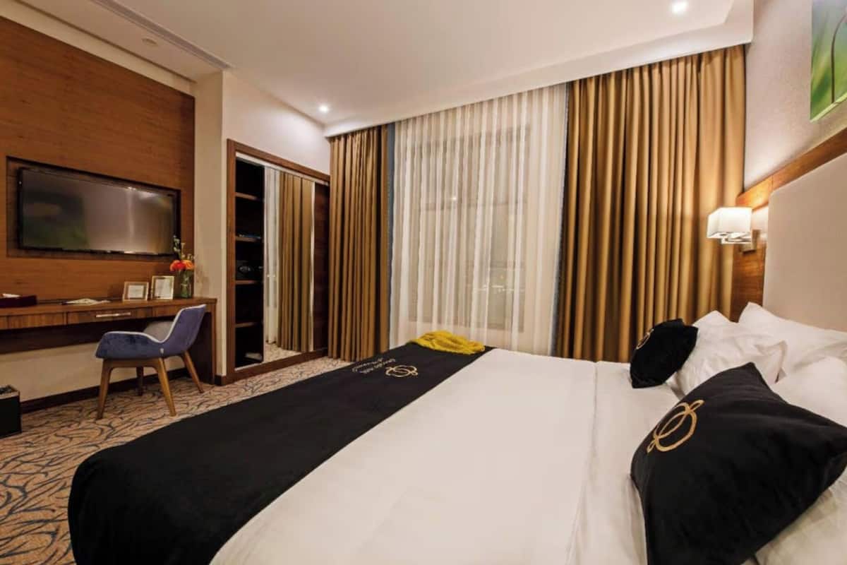 A hotel room with a large bed, a desk with a chair, a television mounted on the wall, and a window with curtains.