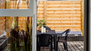 Een terras buiten, met een houten hek, een tafel met stoelen en een potplant.