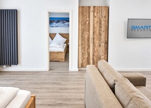Une chambre d’hôtel moderne avec un plancher en bois, un lit recouvert de draps blancs, une grande fenêtre donnant sur un paysage enneigé et un téléviseur fixé au mur.