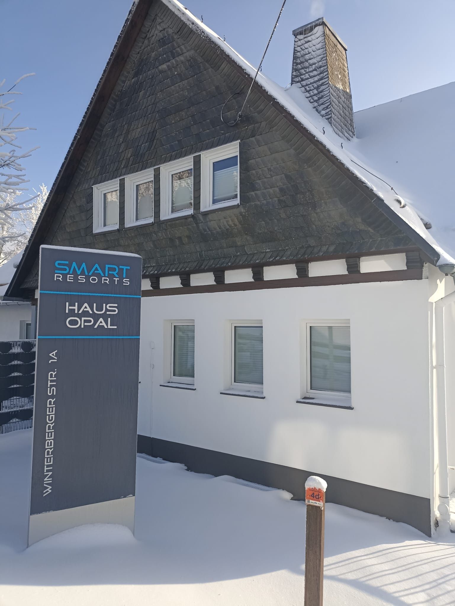 A two-story building with a snow-covered roof and a sign for Smart Resort Haus Opal.