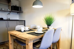 A dining area with a wooden table, four chairs, a potted plant, and a microwave above the cabinets.