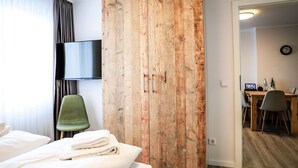 Una camera d'albergo con un paravento in legno, una sedia verde, un letto con lenzuola bianche, una TV a schermo piatto montata a parete e un'area pranzo con tavolo e sedie.