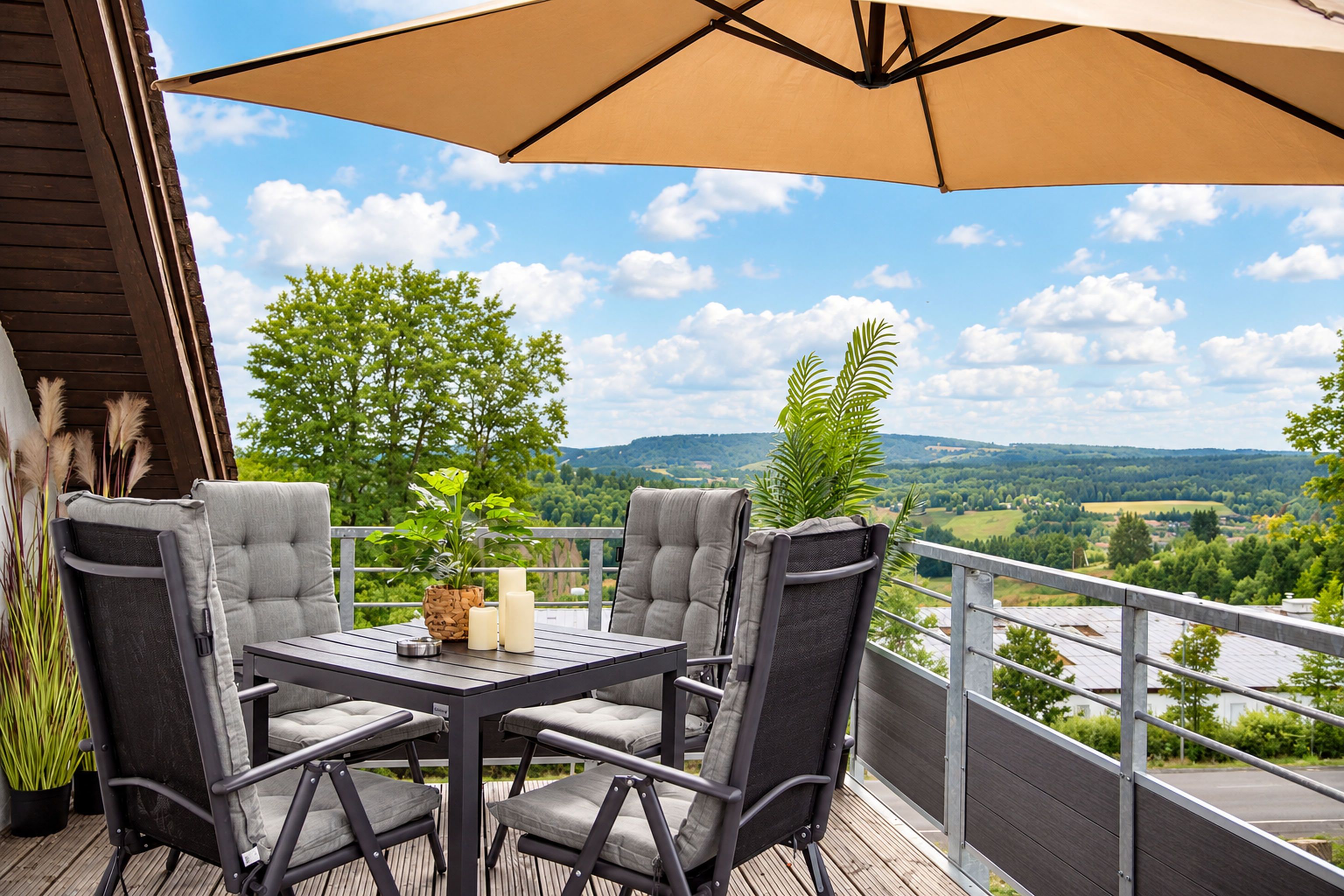 A balcony with a table and chairs, a large umbrella, and a view of a river and hills.