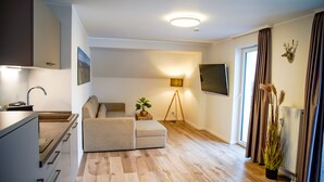 Ein moderner Wohnraum mit Küche, Sofa, Stehlampe und einem an der Wand befestigten Fernseher.