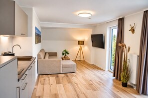 A modern living room with a sofa, a coffee table, a TV mounted on the wall, and a window with curtains.
