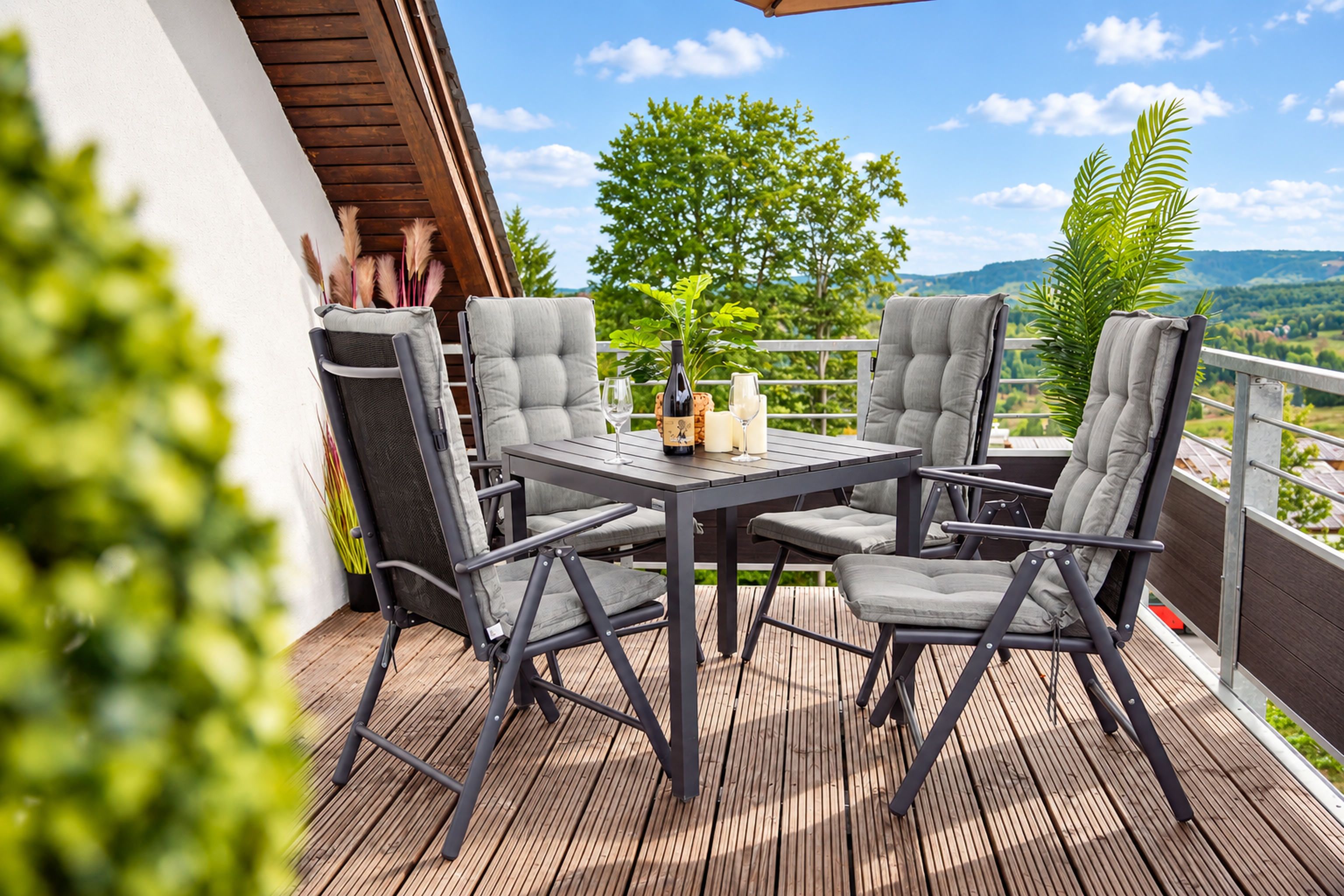 Een terras buiten met een tafel en vier stoelen, een fles wijn en een glas.