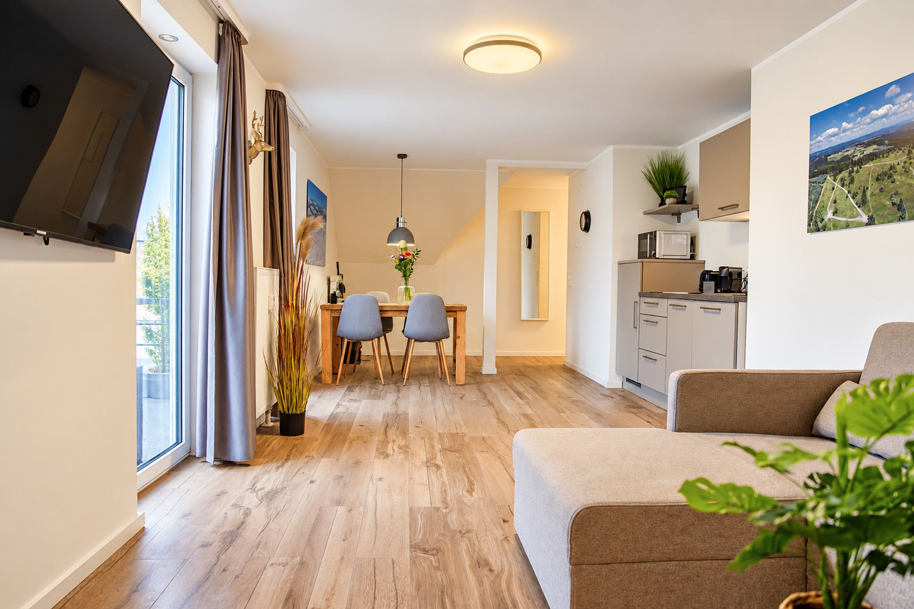 Un salon moderne avec un canapé, un coin repas comprenant une table et des chaises, une cuisine équipée et une grande fenêtre.