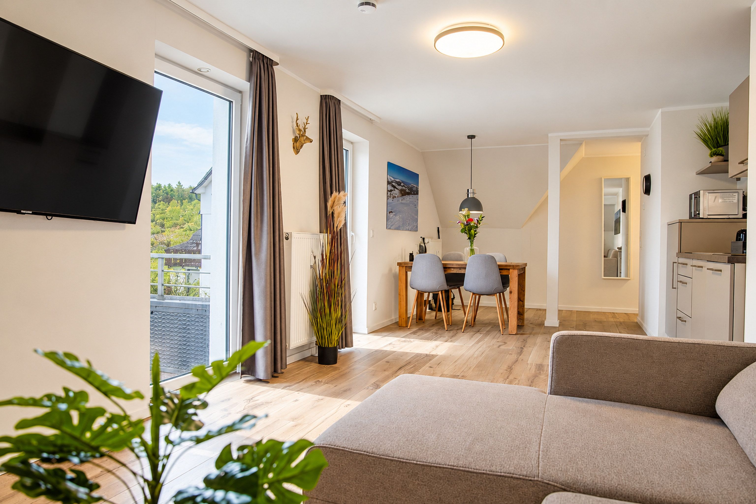 Uma sala de estar moderna com televisão de tela plana, sofá, área de jantar com mesa e cadeiras, e cozinha com micro-ondas.