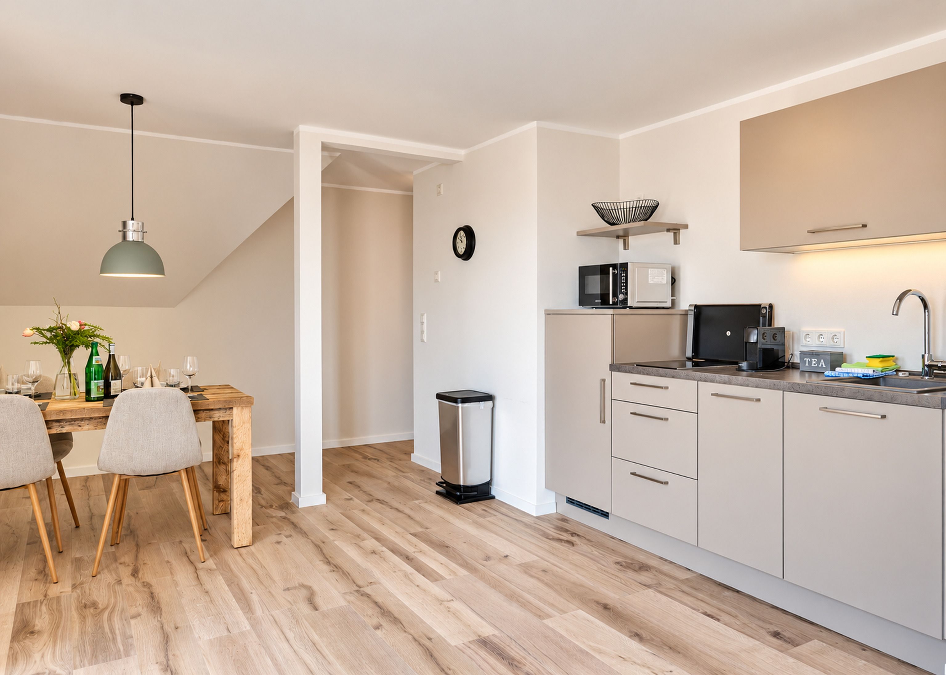 Una cocina moderna con comedor, que incluye una mesa de madera, sillas, un cubo de basura y un microondas.