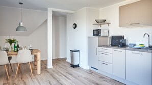 Eine moderne Küche mit weißen Schränken, einer Mikrowelle, einer Kaffeemaschine und einem Spülbecken. Es gibt einen Essbereich mit einem Holztisch und Stühlen.