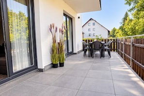 Een balkon met een tafel, stoelen, potplanten en een gebouw op de achtergrond.