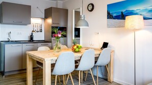 Une cuisine moderne avec un coin repas, comprenant une table en bois, des chaises grises, un vase avec des fleurs et un panier de fruits.