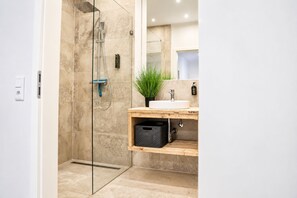 A modern bathroom with a glass-enclosed shower, a wooden vanity, and a potted plant.