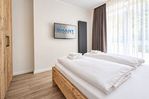 A hotel room with a bed, a TV, and a window with curtains.