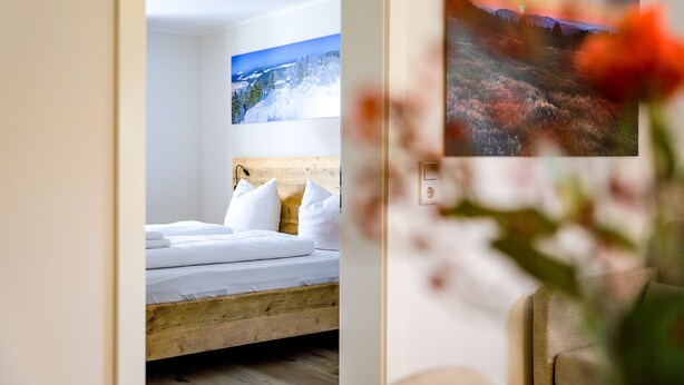 A bedroom with a wooden bed frame, white bedding, and a painting of a snowy landscape above the bed.