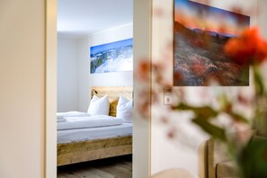 A bedroom with a wooden bed frame, white bedding, and a painting of a snowy landscape above the bed.